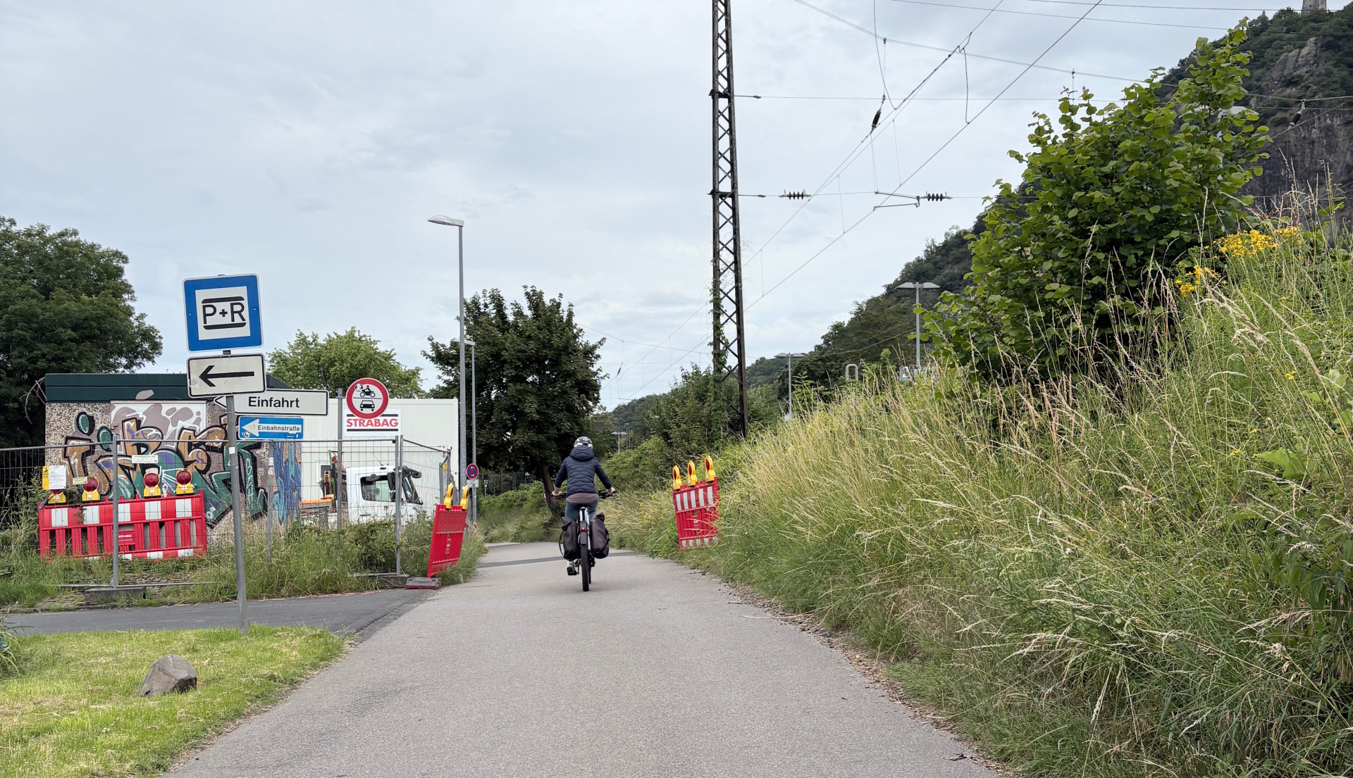 Radfahrerin auf dem Radweg am Bahnhof Rhöndorf neben der Bahnstrecke während der laufenden Modernisierungsarbeiten.