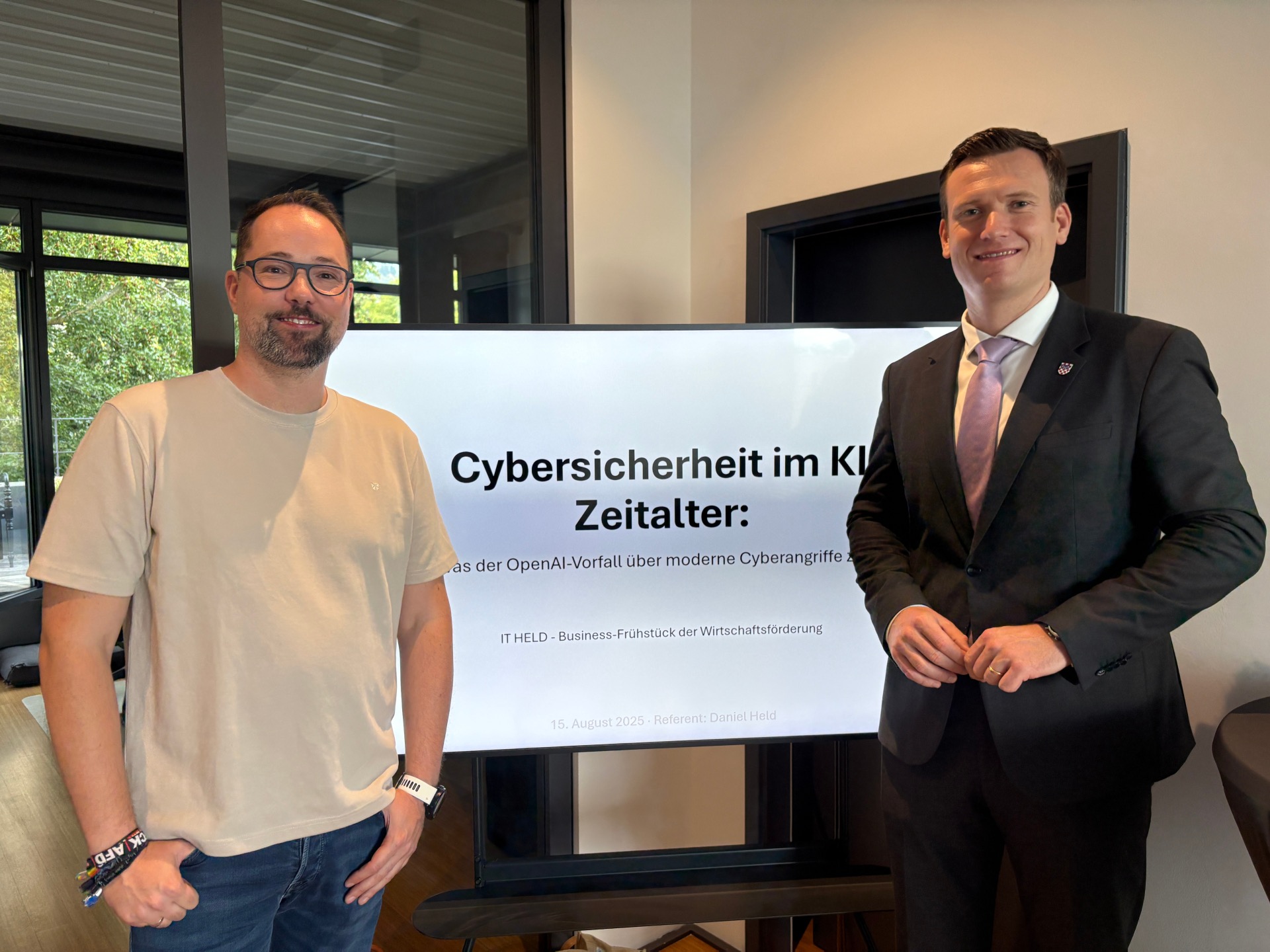 Business-Frühstück IT Held Bürgermeister Philipp Herzog (r.) und Geschäftsführer Daniel Held (l.) stehen vor dem Monitor, der das Thema des Business-Frühstücks zeigt: Cybersicherheit im KI-Zeitalter