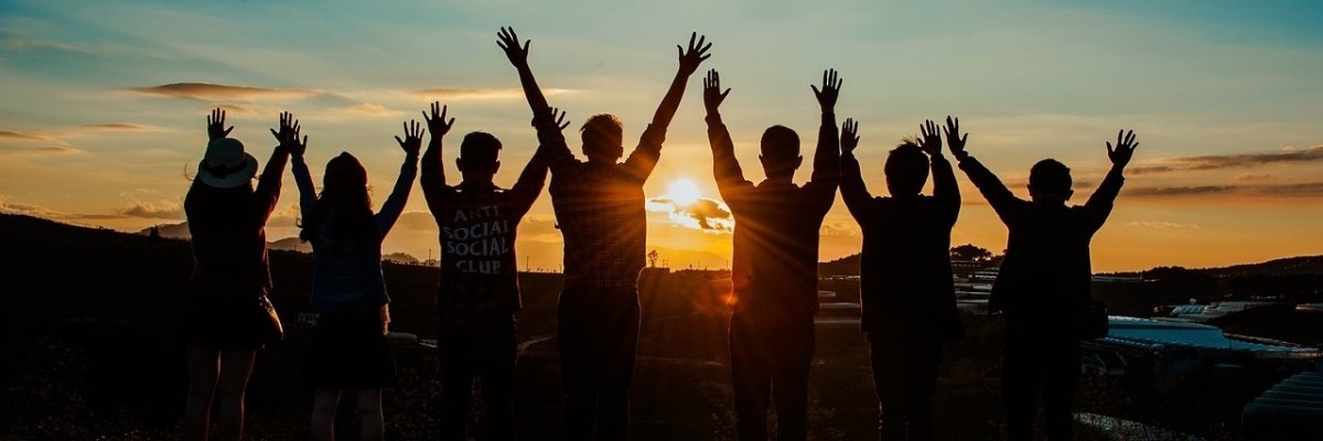 Menschen, die die Arme hochstrecken vor einem Sonnenuntergang