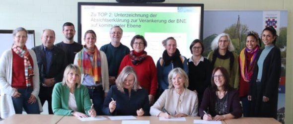 Gruppe von Personen in einem Konferenzraum, vorne sitzen drei Frauen und unterschreiben Dokumente.