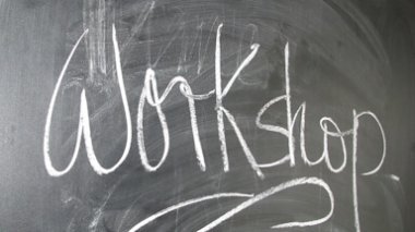 Das Wort ‚Workshop‘ ist mit weißer Kreide groß auf eine dunkle Tafel geschrieben.