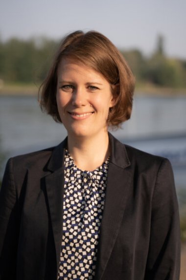Johanna Liel Johanna Liel: Porträt einer Frau mit kurzem hellbraunen Haar, sie trägt ein gemustertes Oberteil und ein dunkles Sakko, im Hintergrund ein Flussufer.