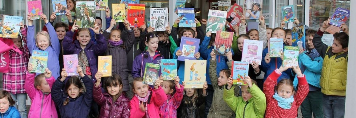Eine Gruppe von Kindern, die Bilder hochhalten und vor der Stadtbücherei stehen