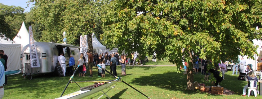 Reitersdorfer Park während Lebensfreudefestival. Im Vordergrund ein Ruderboot des wassersportvereins, im Hintergrund weiße Pagodenzelte sowie Bäume