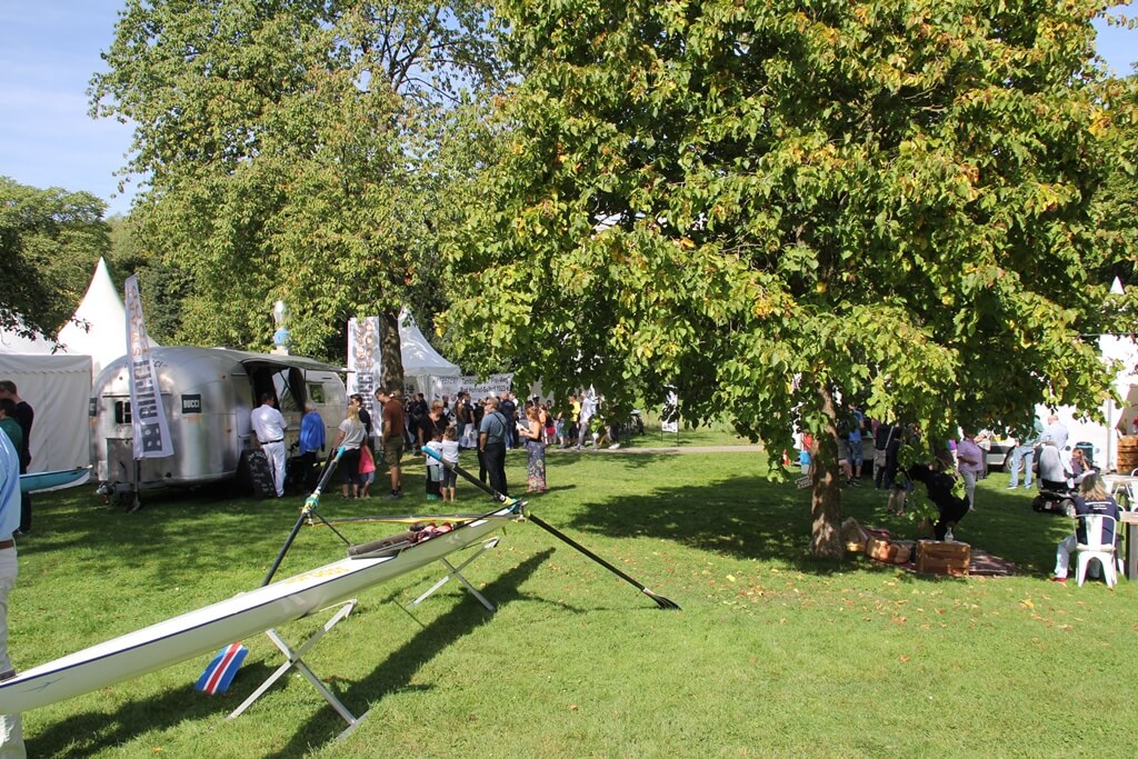 Reitersdorfer Park während Lebensfreudefestival. Im Vordergrund ein Ruderboot des wassersportvereins, im Hintergrund weiße Pagodenzelte sowie Bäume