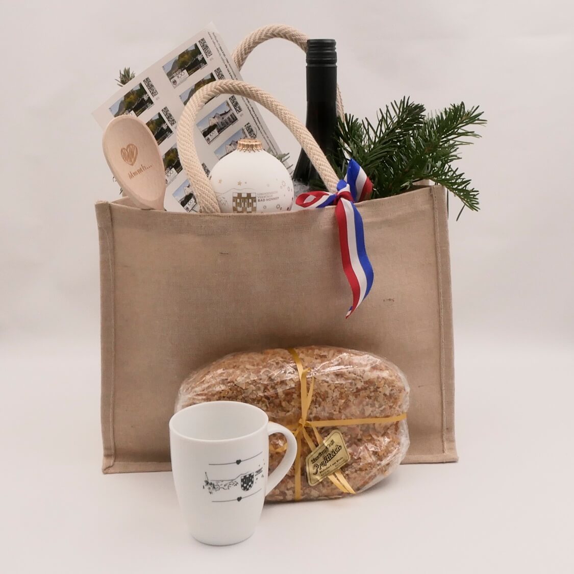 Jutetasche gefüllt mit weihnachtlichen Geschenkideen aus der Bad Honnef-Kollektion: Kochlöffel, Weihnachtsstollen, Weichnachtskugel, Weihnachtstasse, Winzer-Glühwein