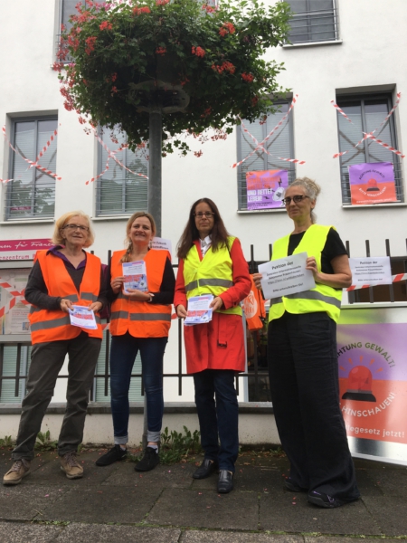 Die Mitarbeiterinnen des Frauenzentrums Bad Honnef und die Gleichstellungsbeauftragte, bekleidet mit Warnwesten, halten Flyer mit Infos zur Protestaktion in den Händen. Ort: Vor dem Frauenzentrum Bad Honnef